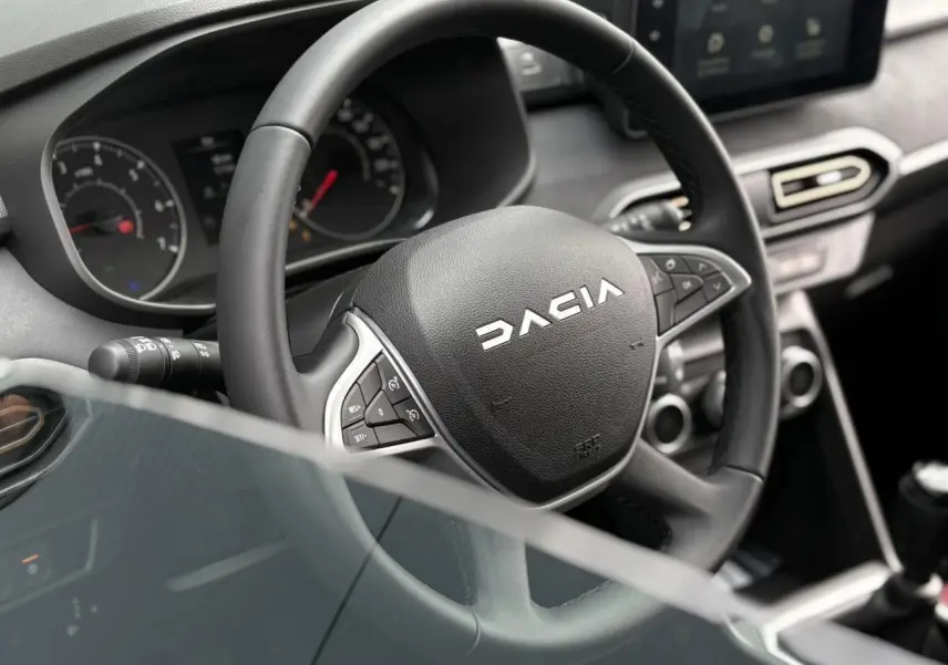 Gros plan sur le volant DACIA du Jogger 2025, avec commandes intégrées et tableau de bord en arrière-plan.