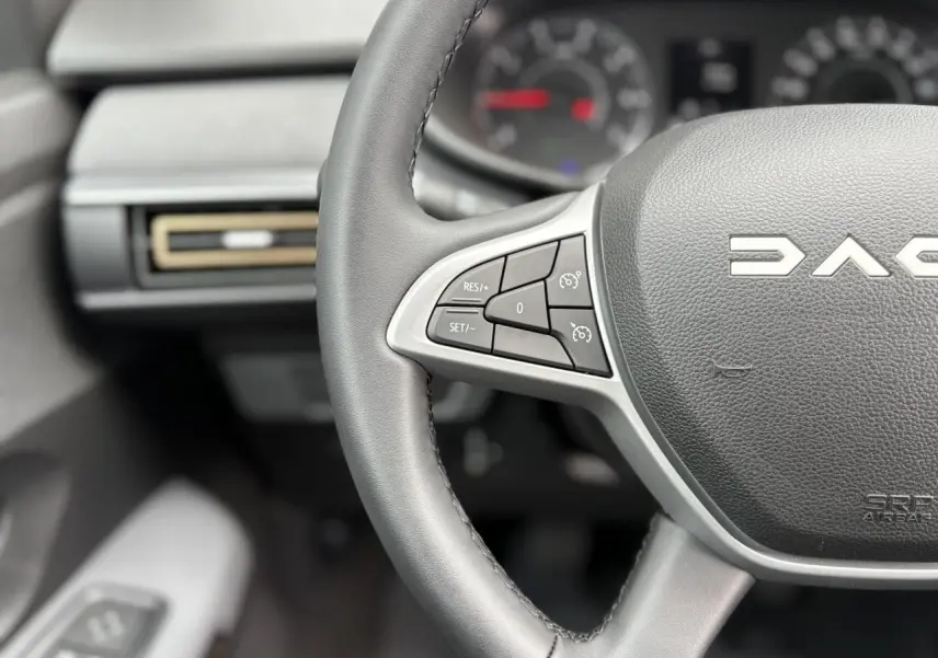 Gros plan sur le volant noir du Dacia Jogger 2025 avec commandes de régulateur de vitesse et tableau de bord flou.