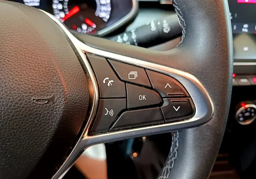 Gros plan sur le côté droit du volant en cuir noir de la Renault Clio Business blanc, avec commandes multifonctions visibles.