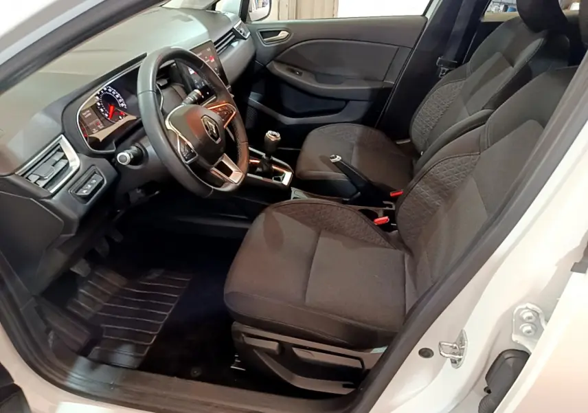 Intérieur côté conducteur d'une Renault Clio blanche 2020, sièges noirs, volant cuir et levier de vitesse manuel visibles.