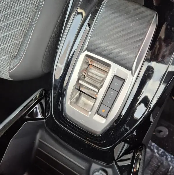 Gros plan sur la console centrale noire brillante de la Peugeot 208 Hybrid 110 Allure, avec sélecteur de boîte automatique et prise 12V.