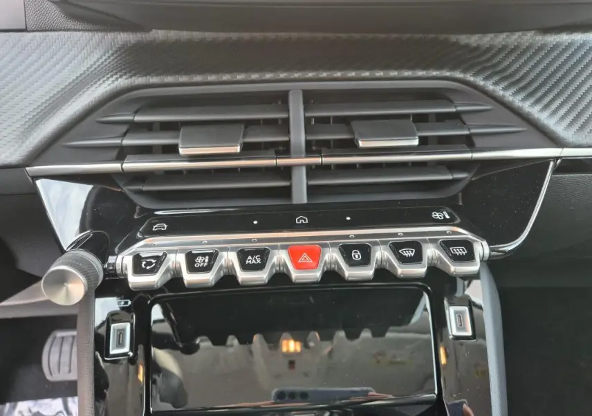 Gros plan sur la console centrale noire brillante de la Peugeot 208 Hybrid 110 Allure 2025, avec boutons de commande et aérateurs.