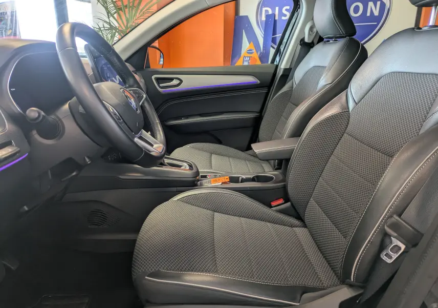 Vue intérieure côté conducteur de la Renault Arkana 1.6 E-Tech noire, avec sièges tissu et cuir et éclairage d'ambiance violet.