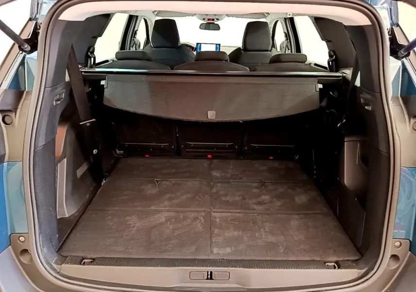 Vue arrière du coffre ouvert du Peugeot 5008 bleu, montrant la tablette cache-bagages et les sièges rabattus.