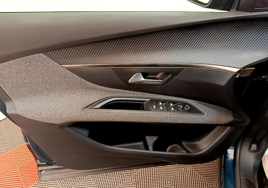 Vue intérieure côté gauche de la porte avant d’un Peugeot 5008 bleu, avec commandes de vitres et poignée argentée.
