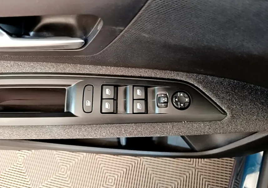 Commande des vitres et rétroviseurs sur la porte côté conducteur d’un Peugeot 5008 bleu, finition tissu gris.