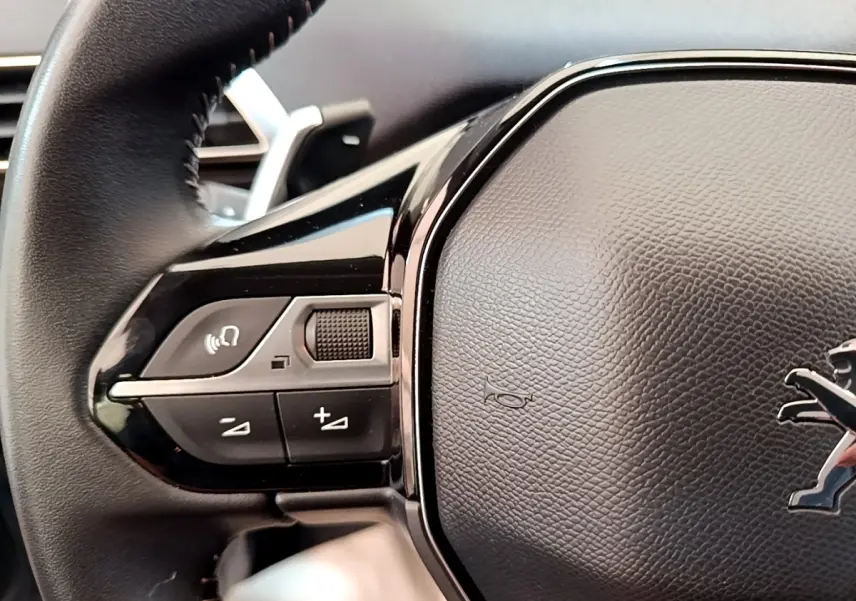 Gros plan sur le volant cuir noir multifonctions du Peugeot 5008 avec commandes audio et logo lion central.