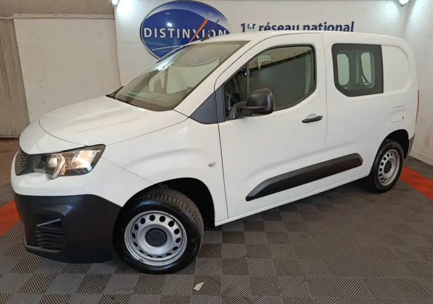 Vue 3/4 avant droit d’un utilitaire Peugeot Partner blanc avec jantes acier et protections noires sur les portes.