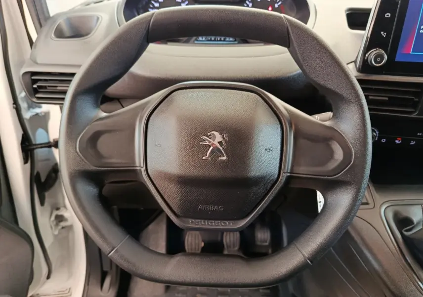 Vue rapprochée du volant noir du Peugeot Partner blanc 2021, avec tableau de bord et levier de vitesse visibles.