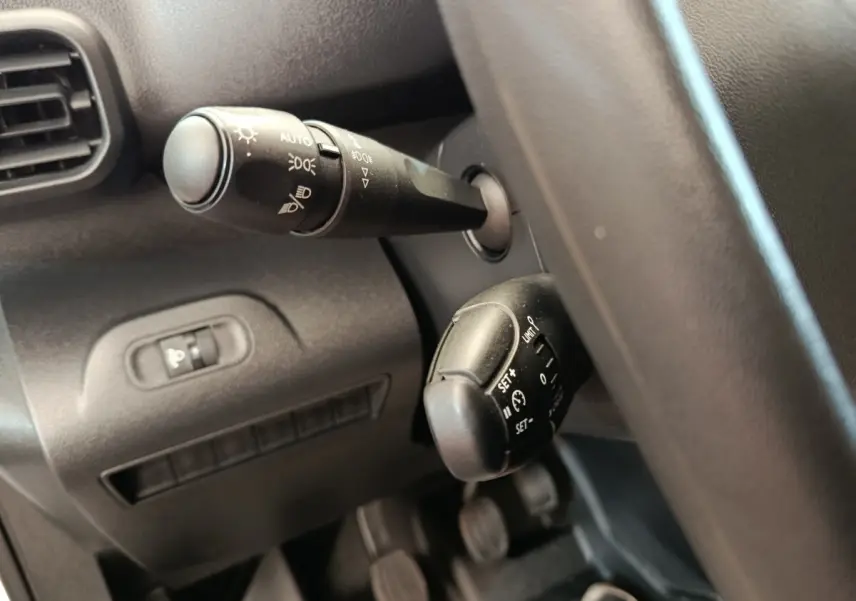 Gros plan sur les commandes de phares et régulateur de vitesse du Peugeot Partner blanc, vue côté conducteur intérieur.
