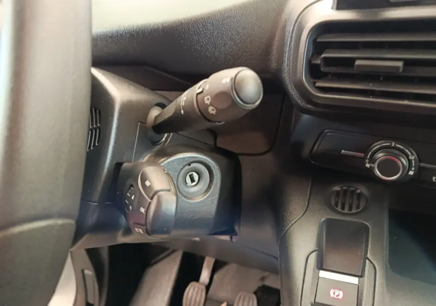 Gros plan sur la colonne de direction et la commande de frein à main électrique dans l'habitacle noir du Peugeot Partner blanc.