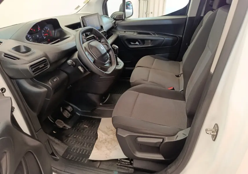 Vue intérieure côté conducteur du Peugeot Partner blanc 2021, montrant le tableau de bord et les sièges avant en tissu gris.