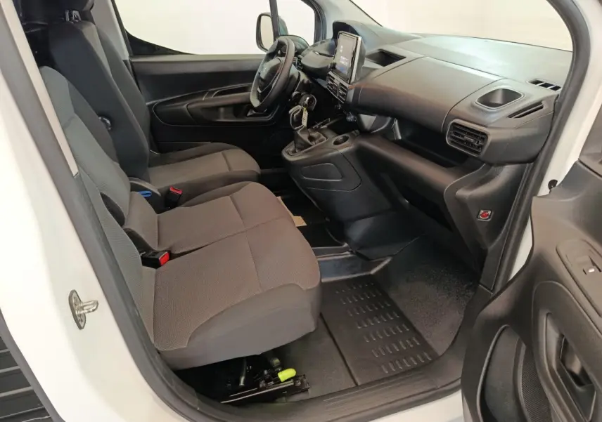 Vue intérieure côté conducteur du Peugeot Partner blanc 2021, montrant les sièges avant et le tableau de bord noir.