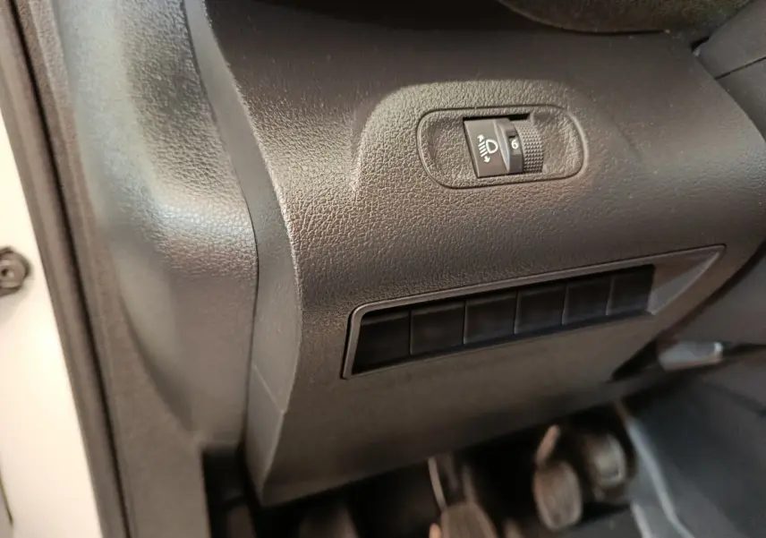 Détail intérieur côté gauche du tableau de bord noir avec commande de réglage des phares du Peugeot Partner blanc.