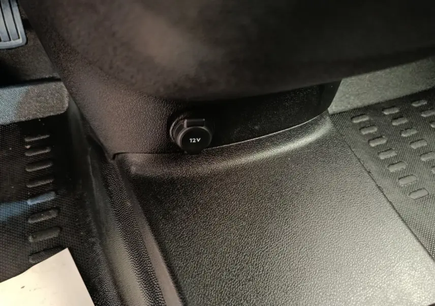 Prise 12V noire sur la console centrale, plancher et tapis en caoutchouc noir du Peugeot Partner blanc 2021.