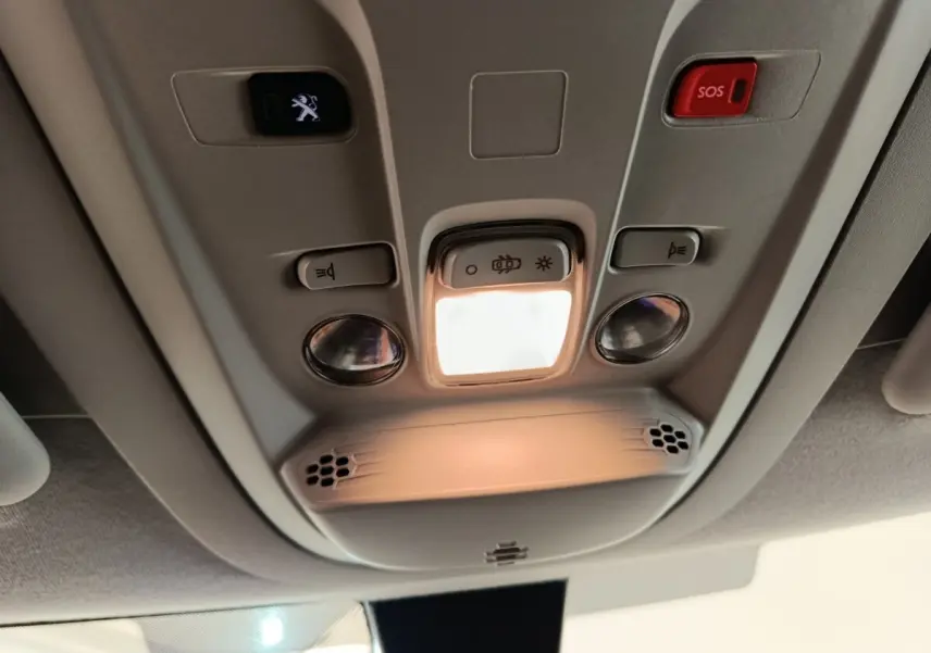 Plafonnier intérieur avec éclairage, boutons de commande et bouton SOS du Peugeot Partner blanc, vue en contre-plongée.