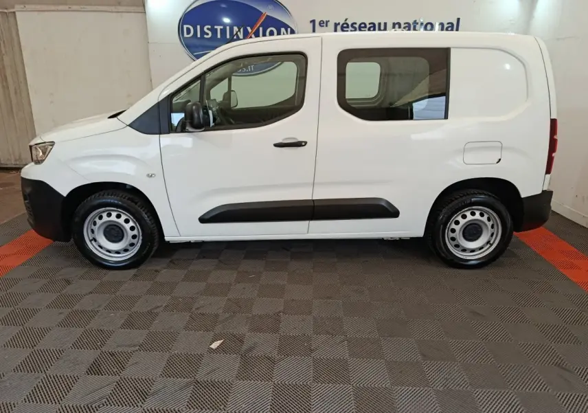 Vue de profil côté gauche d’un Peugeot Partner blanc, utilitaire compact avec porte latérale vitrée et jantes acier.