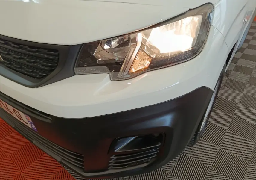 Gros plan sur l'avant droit blanc du Peugeot Partner 2021, phare allumé et pare-chocs noir mat visible.