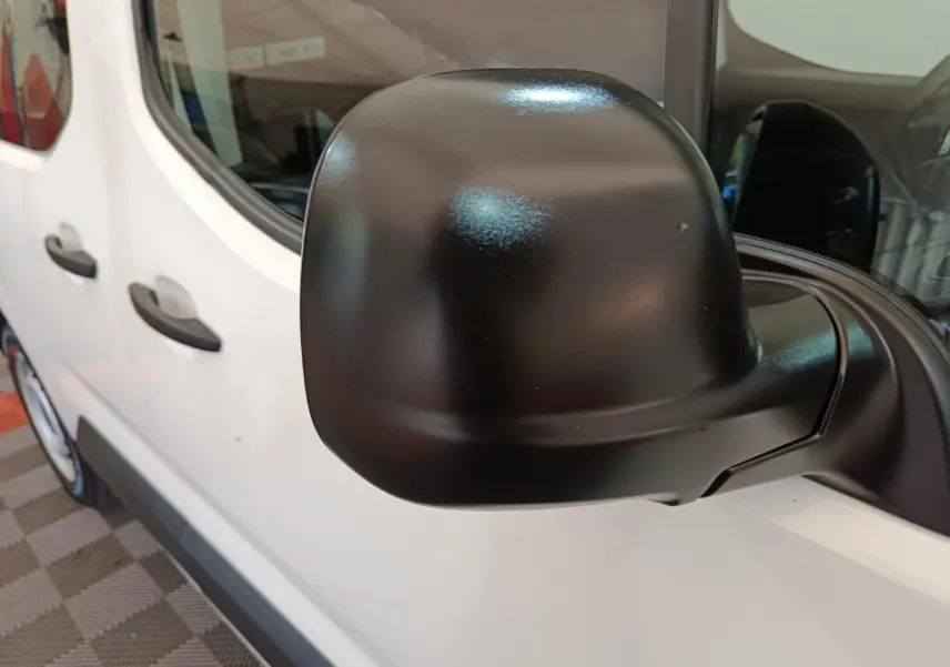 Gros plan sur le rétroviseur noir côté conducteur du Peugeot Partner blanc, vue latérale partielle du véhicule.