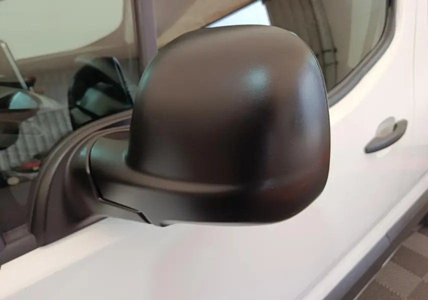 Gros plan sur le rétroviseur noir côté conducteur du Peugeot Partner blanc, avec porte et poignée visibles en arrière-plan.