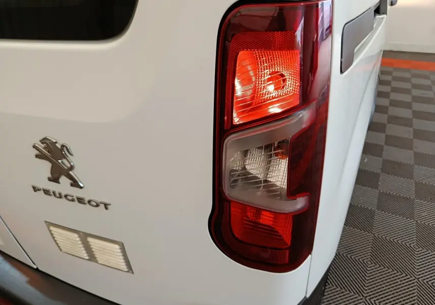 Gros plan sur le feu arrière droit d’un Peugeot Partner blanc, avec logo et partie de la porte arrière visible.