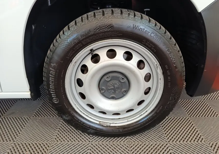Gros plan sur la roue avant gauche blanche en jante acier du Peugeot Partner blanc, avec pneu hiver Continental visible.