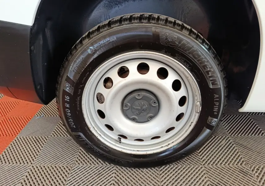 Gros plan sur la roue avant droite blanche d’un Peugeot Partner 2021 avec jante acier et pneu Michelin Alpine.