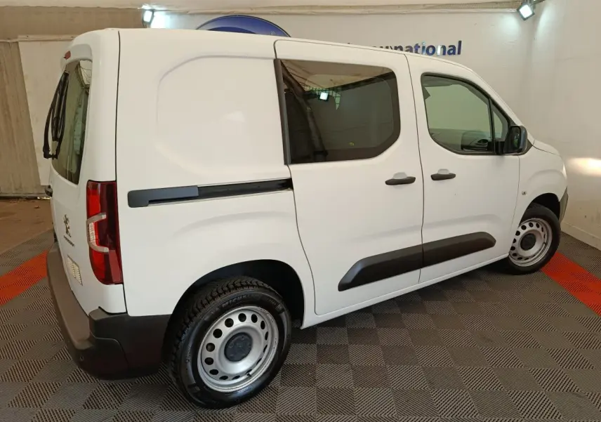 Peugeot Partner blanc vue de profil droit en intérieur, avec vitres teintées et jantes acier simples.