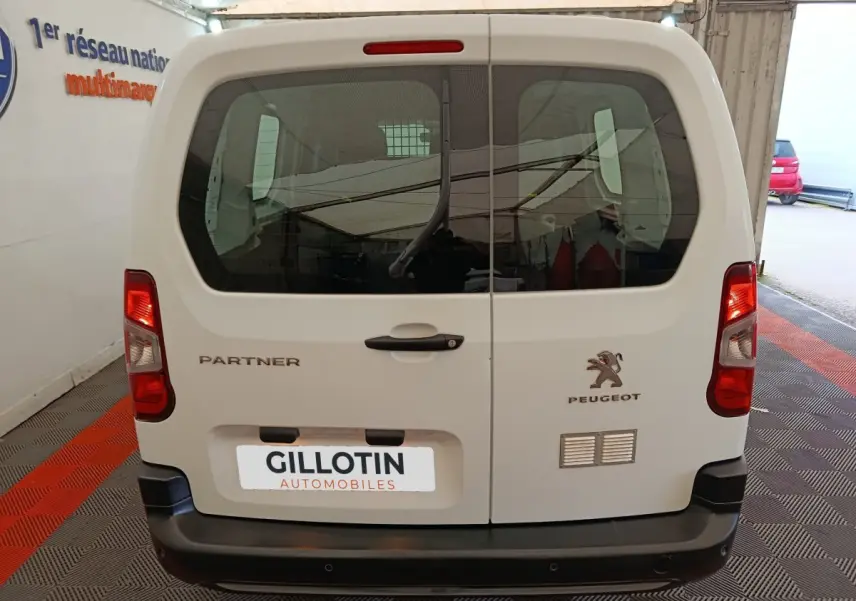 Vue arrière d’un Peugeot Partner blanc 2021 avec portes battantes et logo visible, stationné en intérieur.