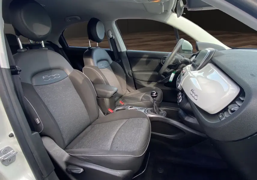 Vue intérieure côté conducteur d'une Fiat 500X blanche, sièges noirs avec logo 500 brodé sur appuie-tête.
