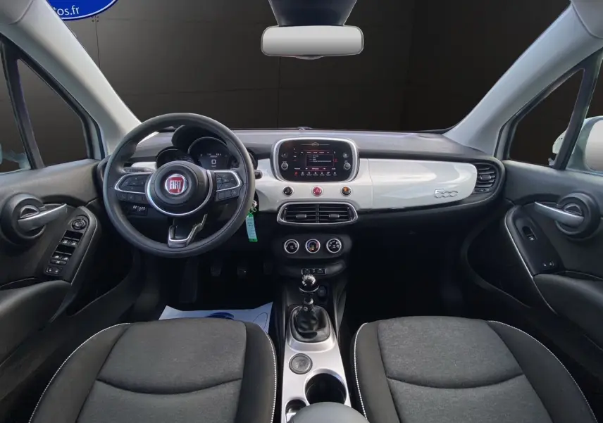 Vue intérieure frontale du tableau de bord blanc et noir de la Fiat 500X 2018 avec volant multifonction et boîte manuelle.