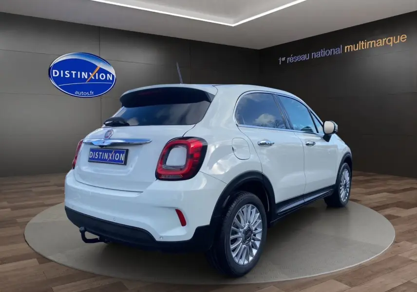 Vue 3/4 arrière droite d'un FIAT 500X blanc avec jantes alliage et feux arrière LED dans un showroom.