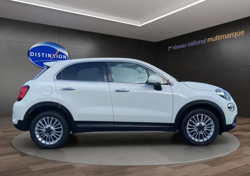 Profil côté gauche d'un FIAT 500X blanc 2018 avec jantes alliage et détails noirs urbains en intérieur showroom.