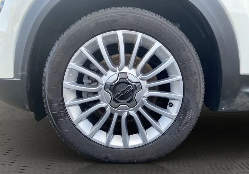 Gros plan sur la roue avant droite blanche d'une Fiat 500X 2018 avec jante alliage argentée au design étoilé.