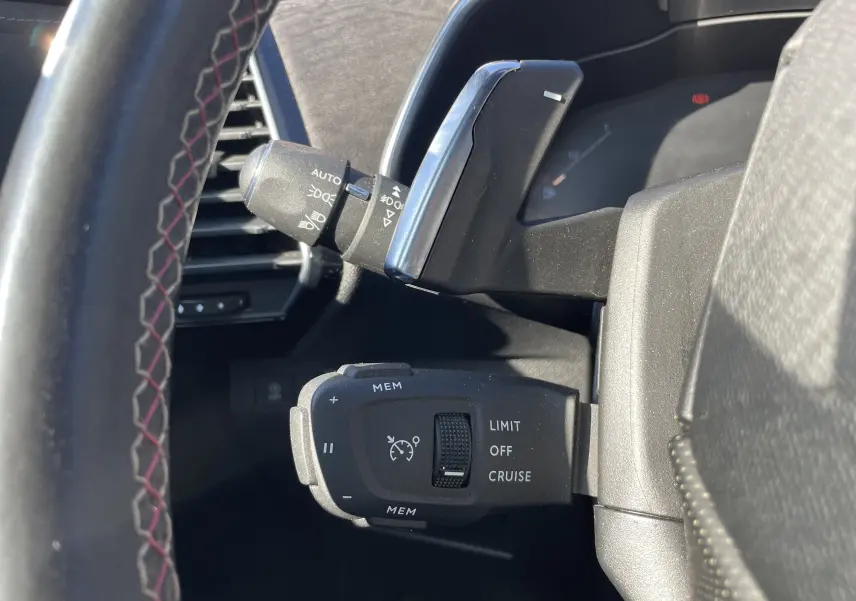 Gros plan sur les commandes de régulateur de vitesse et éclairage à gauche du volant du DS7 gris, intérieur noir.