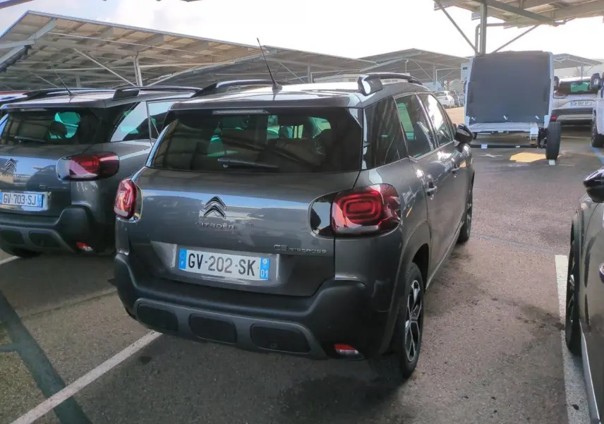 Vue 3/4 arrière droite d'un Citroën C3 Aircross gris foncé avec jantes alliage et barres de toit noires.