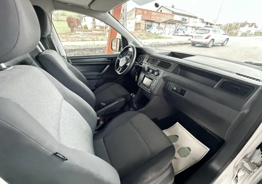 Vue intérieure côté conducteur du Volkswagen Caddy blanc 2017, montrant les sièges noirs et la planche de bord simple.