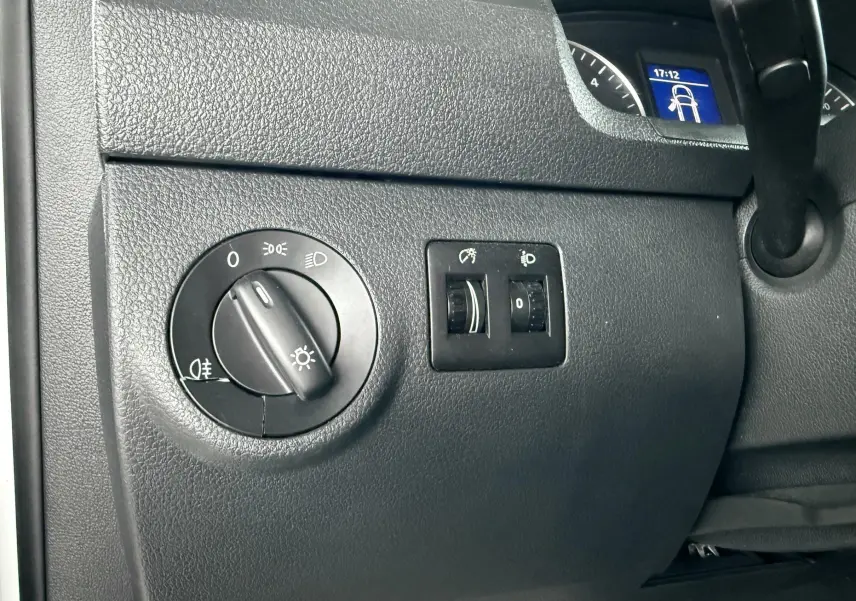 Gros plan sur le tableau de bord noir du Volkswagen Caddy, montrant les commandes d’éclairage et un écran digital partiel.