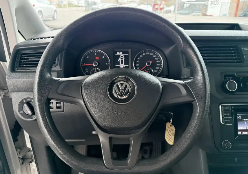 Vue intérieure centrée sur le volant noir avec logo Volkswagen du Volkswagen Caddy Maxi Long blanc, tableau de bord visible.