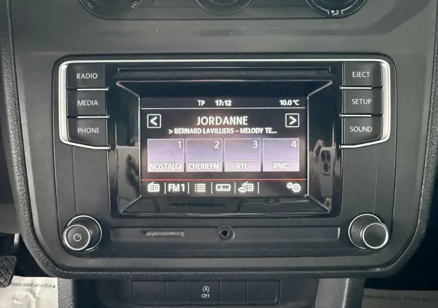 Gros plan sur l’écran multimédia noir du Volkswagen Caddy Maxi Long 2017 affichant une radio FM avec plusieurs stations.