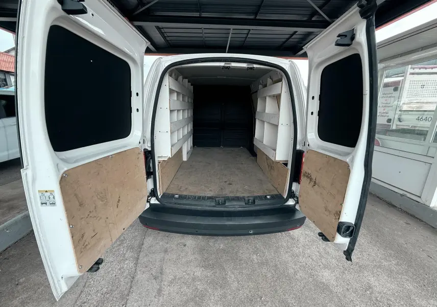 Vue arrière du Volkswagen Caddy Maxi Long blanc 2017 avec portes ouvertes montrant l'intérieur aménagé avec étagères blanches.