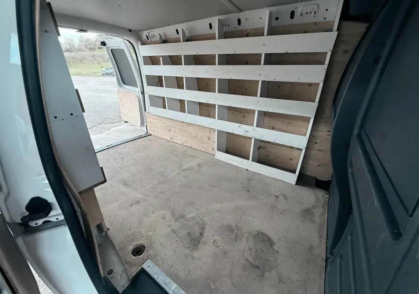 Vue intérieure arrière du Volkswagen Caddy Maxi Long blanc, montrant l'espace de chargement avec étagères en bois sur le côté droit.