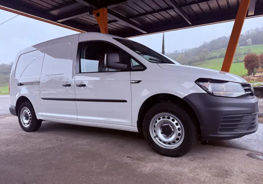 Vue 3/4 avant droit d’un Volkswagen Caddy Maxi Long blanc avec pare-chocs noirs sous un abri en milieu rural.