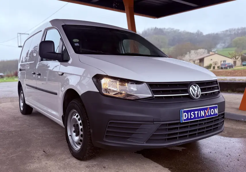 Vue 3/4 avant droit d'un Volkswagen Caddy Maxi Long blanc avec pare-chocs noir mat sous un abri.