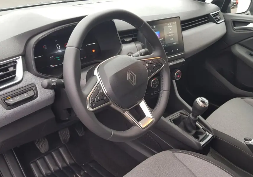 Vue intérieure côté conducteur de la Renault Clio gris 2025, avec volant multifonction et boîte manuelle visible.