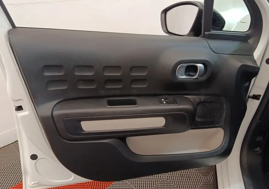 Vue rapprochée de la porte avant gauche blanche d'une Citroën C3 avec panneau intérieur noir et beige.