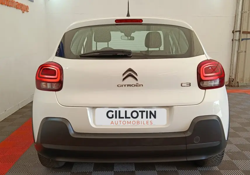 Vue arrière d'une Citroën C3 blanche 2022 avec feux arrière LED et pare-chocs noir mat en intérieur showroom.