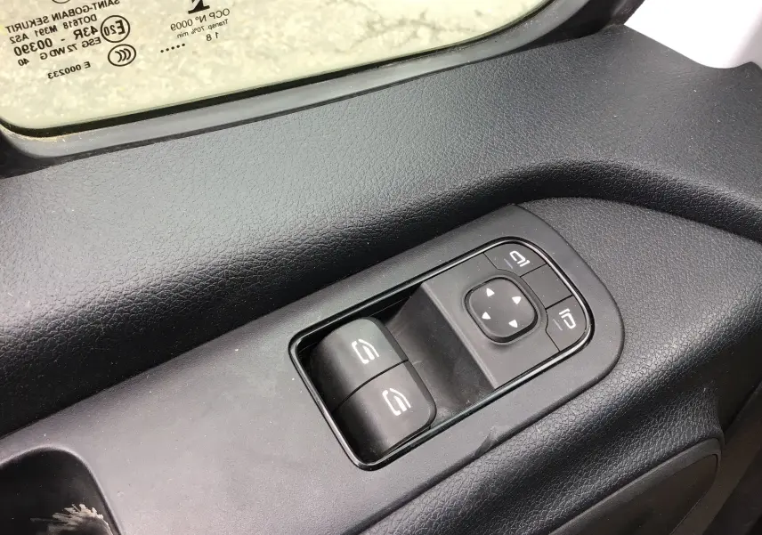 Gros plan sur les commandes électriques des vitres côté conducteur d'un Mercedes Sprinter blanc, intérieur noir.