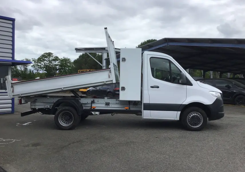 Vue de profil côté droit d'un Mercedes Sprinter blanc avec benne relevée et coffre latéral blanc.