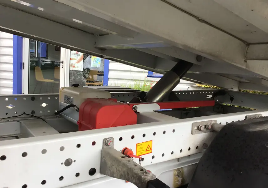 Gros plan sous la benne du Mercedes Sprinter blanc, montrant le mécanisme hydraulique et le châssis perforé.